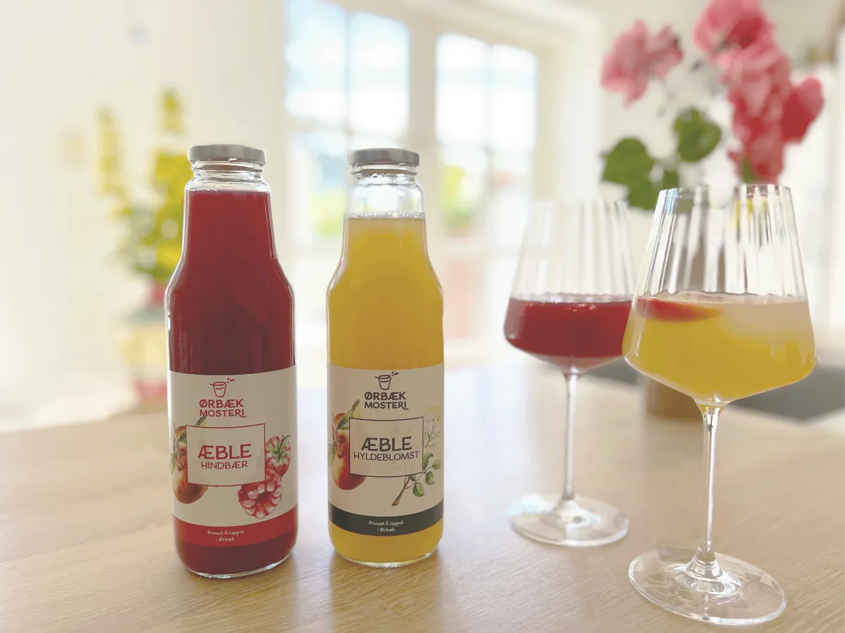 Ørbæk Mosteris flasker med hindbær- og hyldeblomstsaft på et køkkenbord
